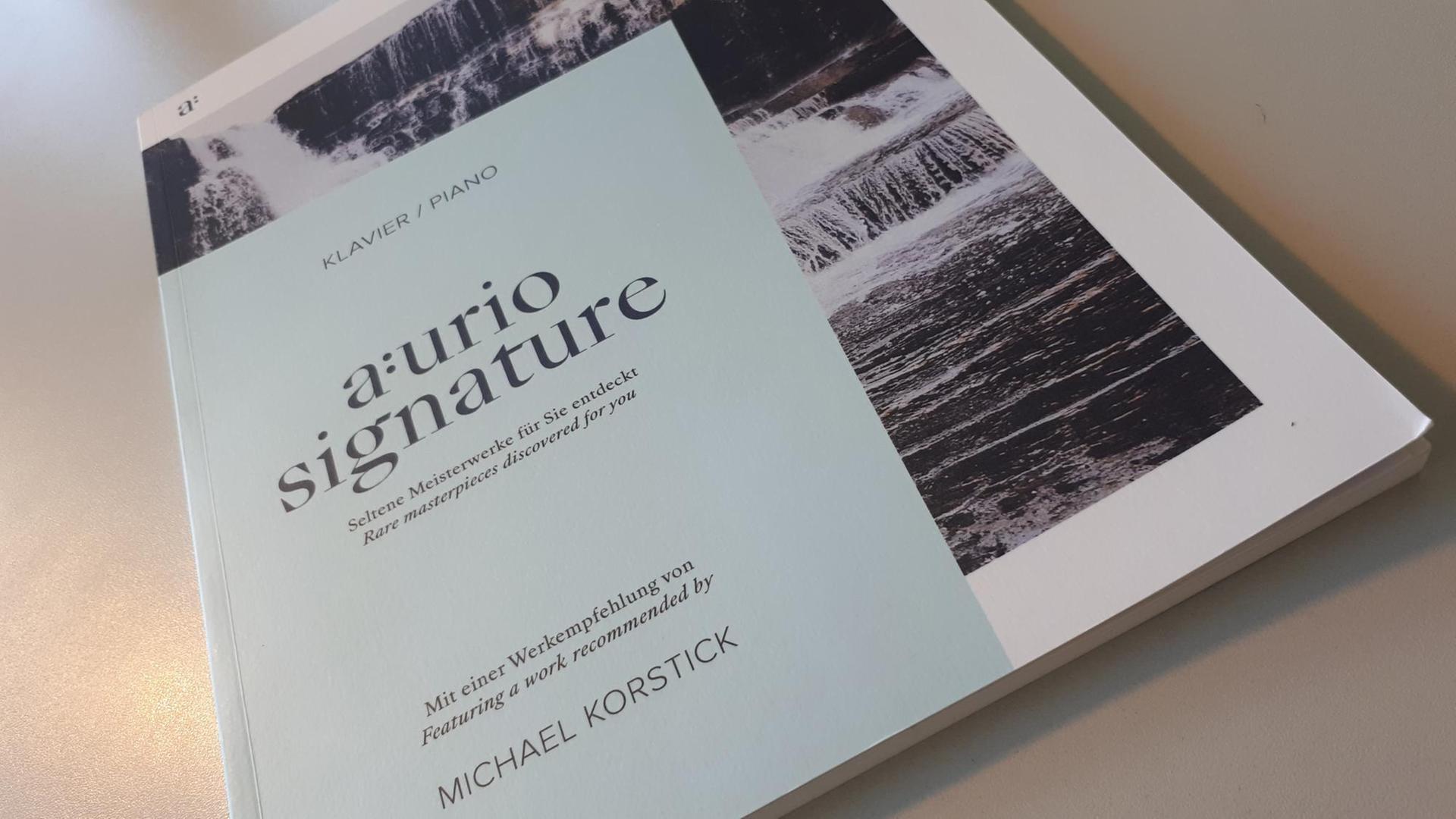 Auf einer Tischplatte liegt ein helles Magazin, auf dem "aurio signature" steht. Auf einer Tischplatte liegt ein helles Magazin, auf dem "aurio signature" steht.