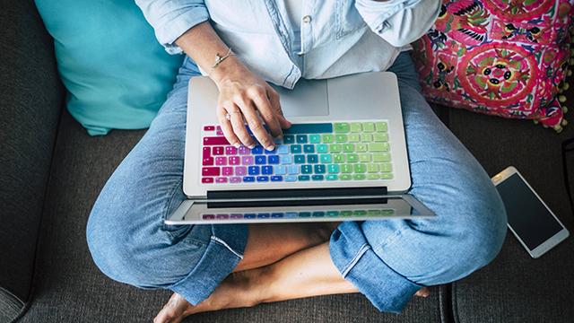 Woman using laptop with multicoloured keyboard on couch at home model released Symbolfoto property released PUBLICATIONxINxGERxSUIxAUTxHUNxONLY SIPF01961