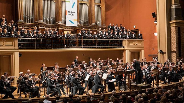 Ein Blick auf die Bühne mit groß besetztem Orchester und Chor auf der Bühnenempore. Ein Blick auf die Bühne mit groß besetztem Orchester und Chor auf der Bühnenempore.