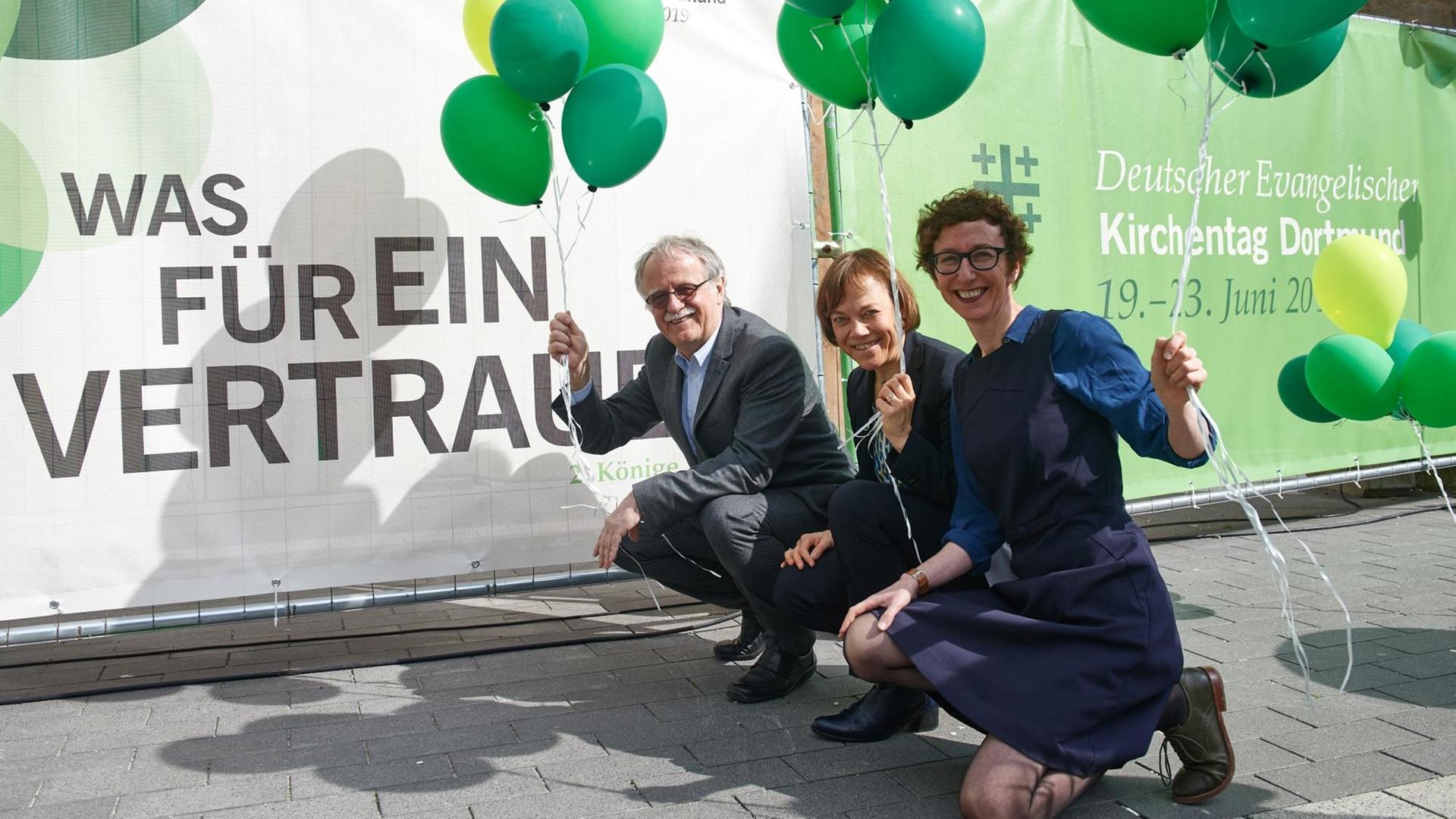 16.04.2018, Nordrhein-Westfalen, Dortmund: Kirchentagspräsident Hans Leyendecker, Präses Annette Kurschus und Generalsekretärin Julia Helmke (v.l.n.r.) mit Luftballons vor einem Plakat für den Deutschen Evangelischen Kirchentags, der vom 19. bis 23. Juni in Dortmund stattfindet 16.04.2018, Nordrhein-Westfalen, Dortmund: Kirchentagspräsident Hans Leyendecker, Präses Annette Kurschus und Generalsekretärin Julia Helmke (v.l.n.r.) mit Luftballons vor einem Plakat für den Deutschen Evangelischen Kirchentags, der vom 19. bis 23. Juni in Dortmund stattfindet
