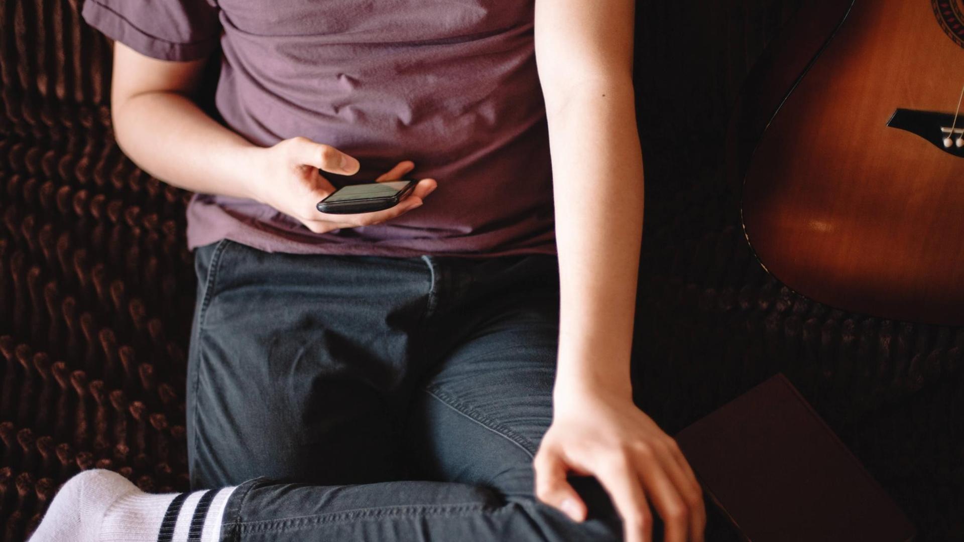 Ein Jugendlicher sitzt auf einem Sofa und benutzt ein Smartphone Ein Jugendlicher sitzt auf einem Sofa und benutzt ein Smartphone