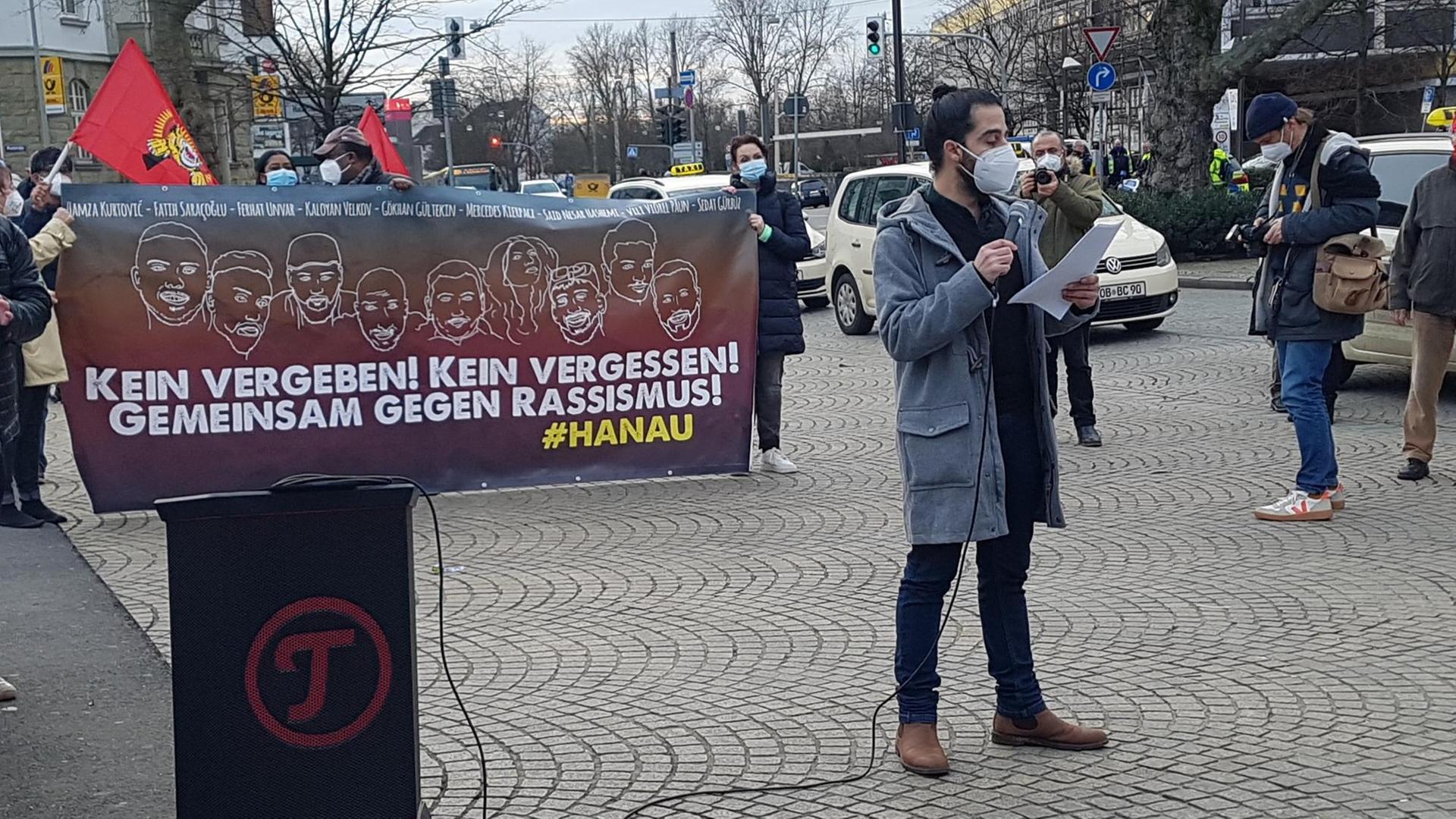 Ein Mann im grauen Dufflecoat trägt Mundschutz, während er bei einer Demonstration einen Text vorliest. Ein Mann im grauen Dufflecoat trägt Mundschutz, während er bei einer Demonstration einen Text vorliest.