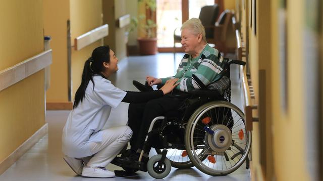 Junge Chinesin in weißer Kleidung spricht mit einer älteren Frau im Rollstuhl
