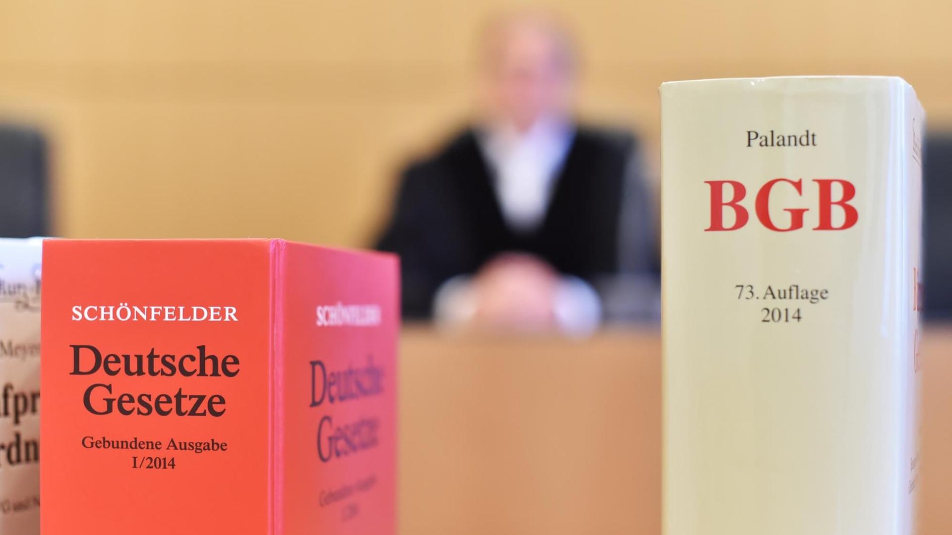 An der Richterbank eines Sitzungssaals sitzt ein Richter mit Richterrobe, davor stehen Gesetzesbücher. An der Richterbank eines Sitzungssaals sitzt ein Richter mit Richterrobe, davor stehen Gesetzesbücher.