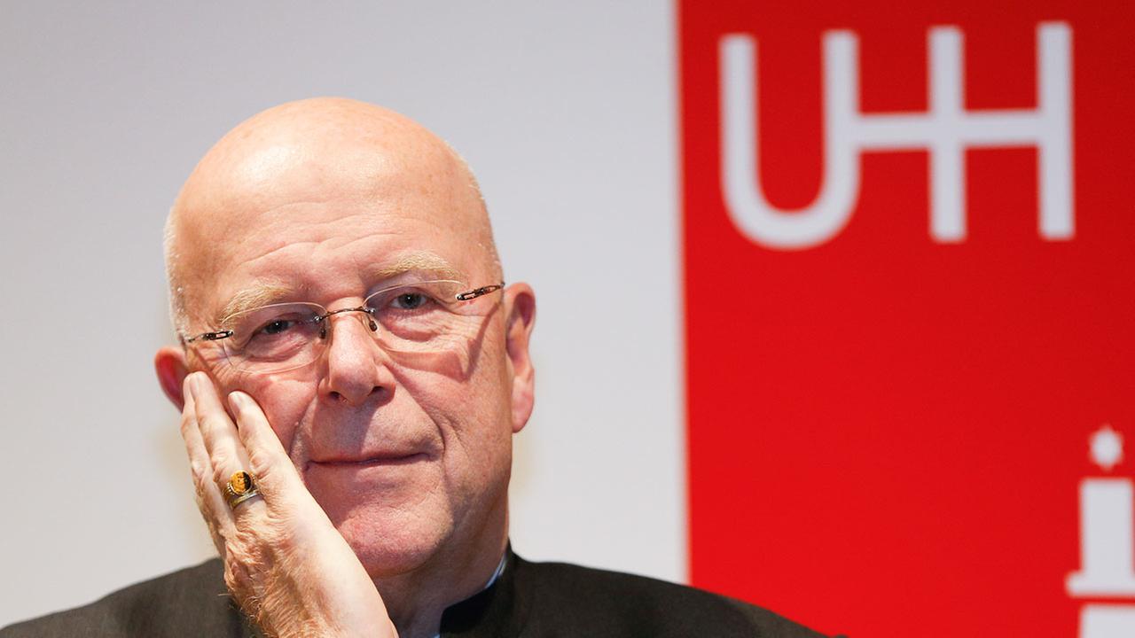 Der Präsident der Universität Hamburg, Dieter Lenzen, im Porträt. Er stützt eine Hand im Gesicht auf, im Hintergrund ist ein rotes Plakat zu sehen.