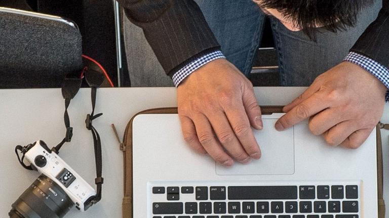 Ein Mann sitzt an einem Computer, daneben eine Kamera. Ein Mann sitzt an einem Computer, daneben eine Kamera.