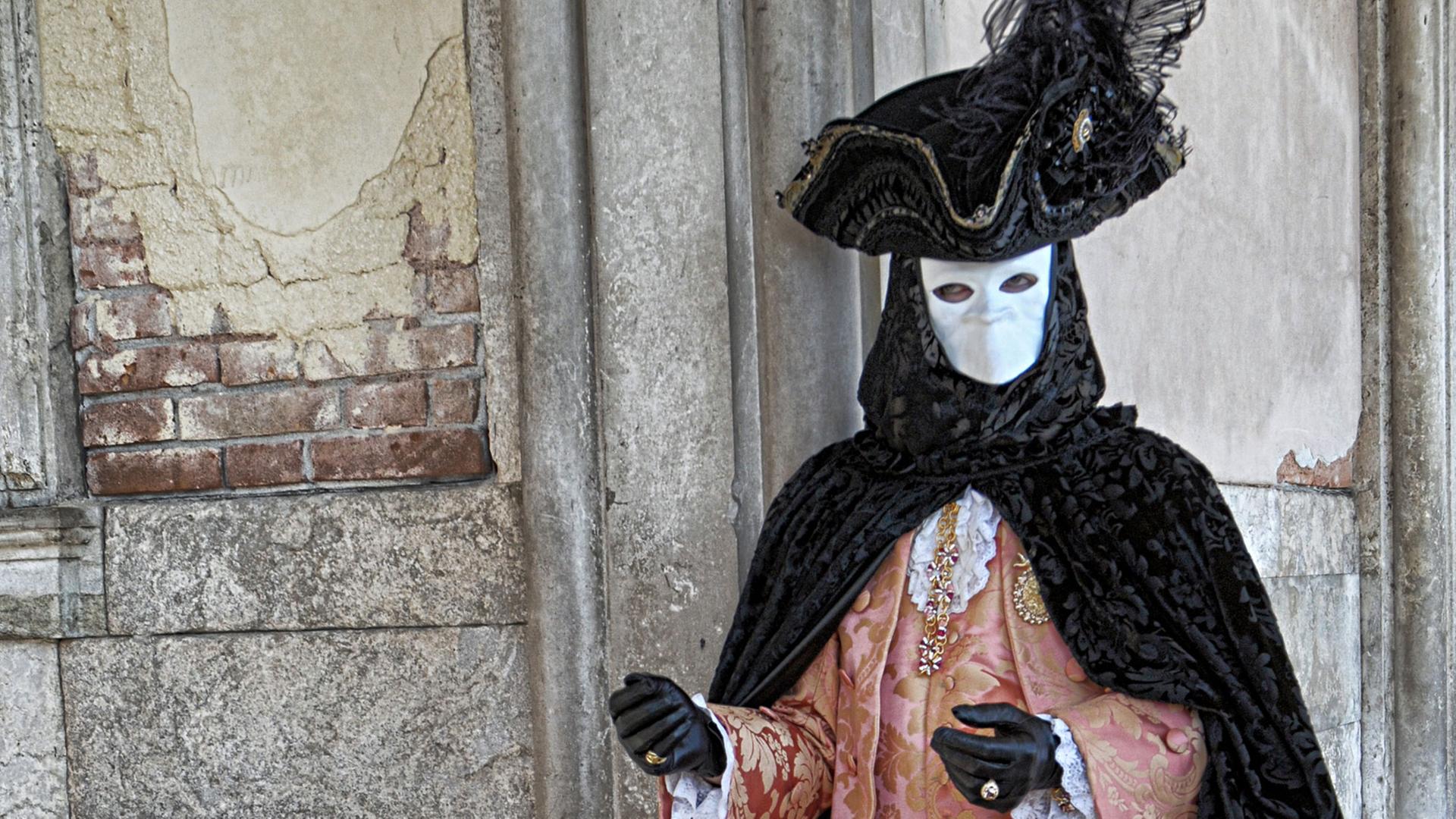 Eine maskierte und kostümierte Person posiert beim Karneval in Venedig.