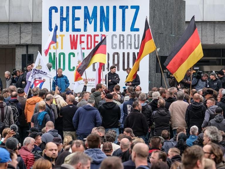 Demonstranten stehen in Chemnitz vor der Karl-Marx-Statue. Darauf ein Spruchband: "Chemnitz ist weder grau noch braun."