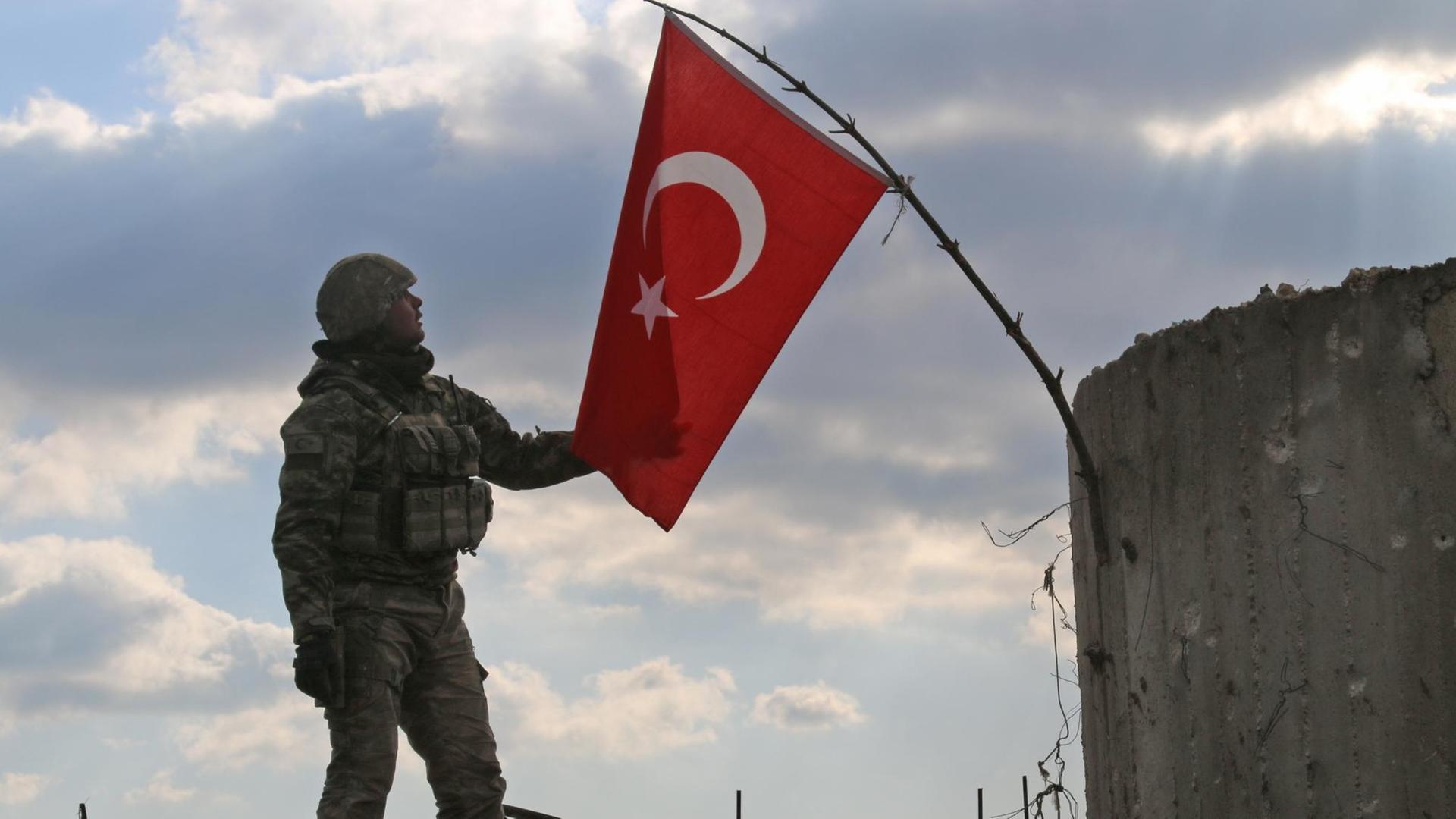 A Turkish soldier checks the national flag on a mountain on the Syrian-Turkish border, north of Azaz on January 28, 2018. Turkey launched operation "Olive Branch" on January 20 against the Syrian Kurdish People's Protection Units (YPG) militia in Afrin, supporting Syrian opposition fighters with ground troops and air strikes. / AFP PHOTO / Maan al-SHANAN