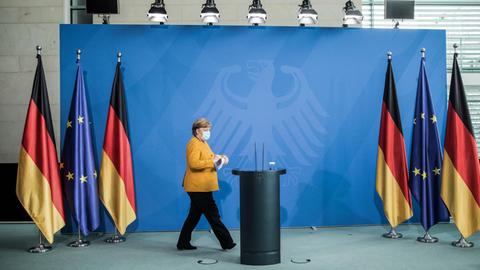 Angela Merkel läuft in einer senfgelben Jacke zum Rednerpult.