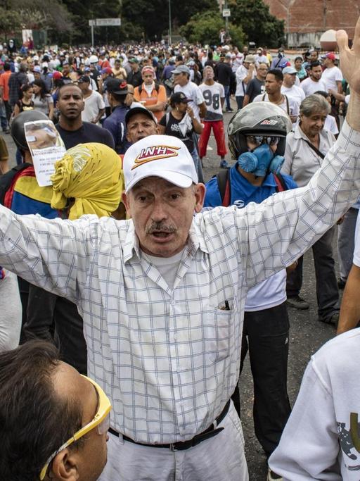 Ein Mann hebt die Arme hoch bei einem Protest gegen die Regierung von Präsidenten Maduro.