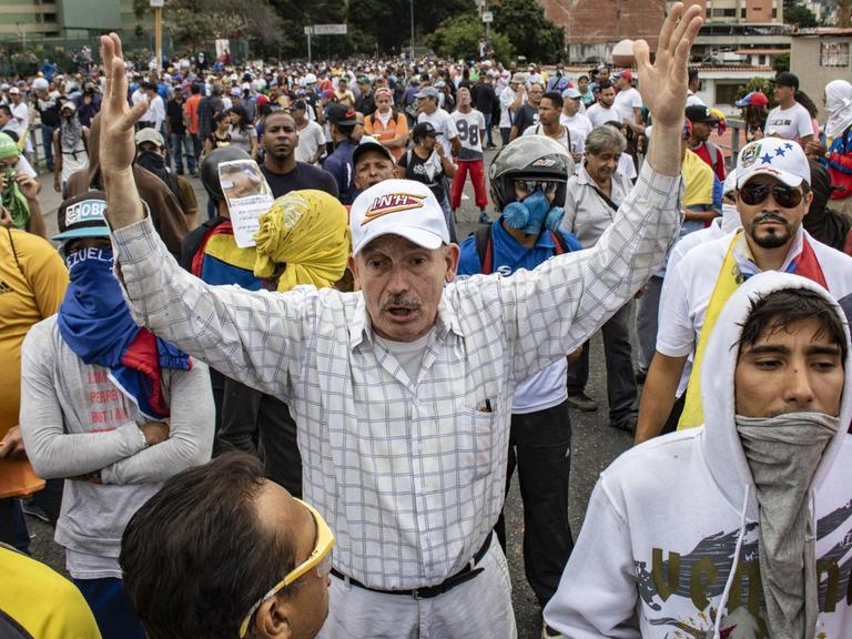Ein Mann hebt die Arme hoch bei einem Protest gegen die Regierung von Präsidenten Maduro.