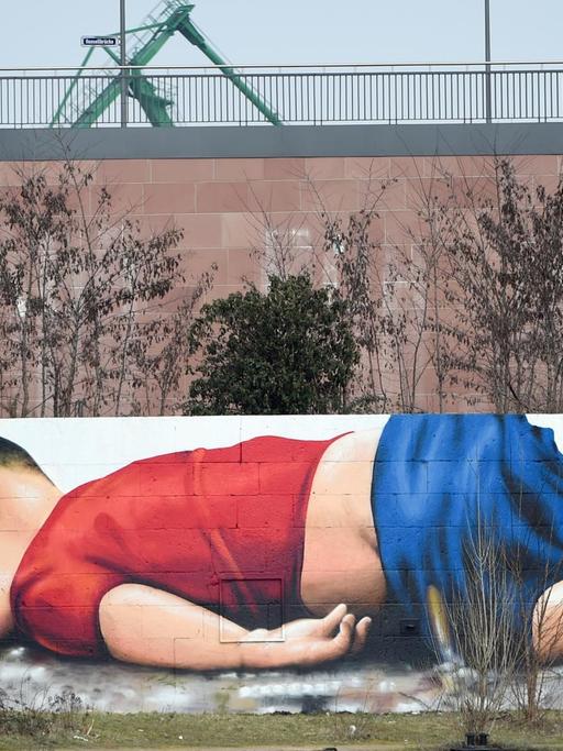 Das Foto des ertrunkenen syrischen Flüchtlingskindes Aylan Kurdi dient als Vorlage für ein gesellschaftskritisches Graffiti, das am 11.03.2016 auf der Osthafenmole in Frankfurt am Main (Hessen) zu sehen ist. Rund 40 Stunden haben die Künstler Justus Becker und Oguz Sen an dem rund 120 Quadratmeter großen Motiv gearbeitet. Foto: Arne Dedert/dpa | Verwendung weltweit