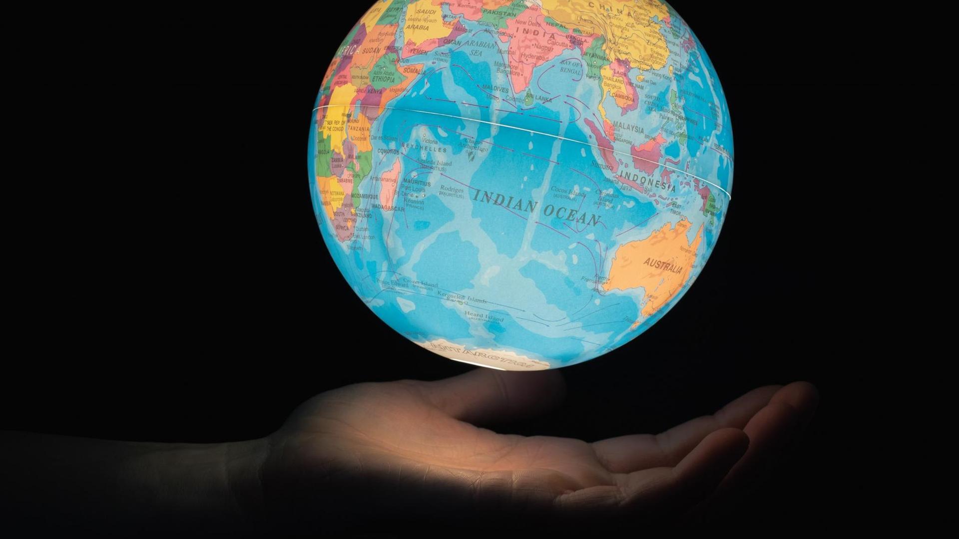 Ein beleuchteter Globus vor dunklem Hintergrund scheint über einer geöffneten Hand zu schweben Ein beleuchteter Globus vor dunklem Hintergrund scheint über einer geöffneten Hand zu schweben