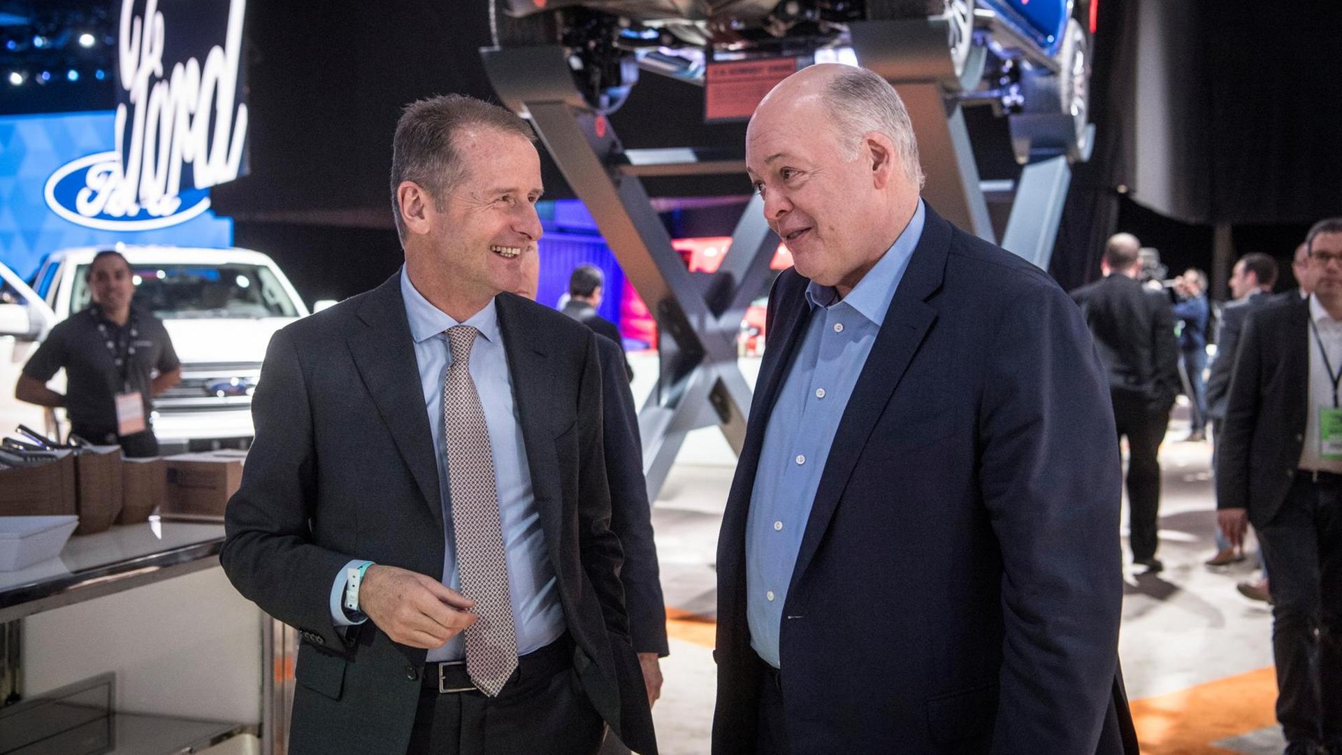 Die beiden unterhalten sich lächelnd am Ford-Stand vor einem Automodell auf einem Podest. Die beiden unterhalten sich lächelnd am Ford-Stand vor einem Automodell auf einem Podest.