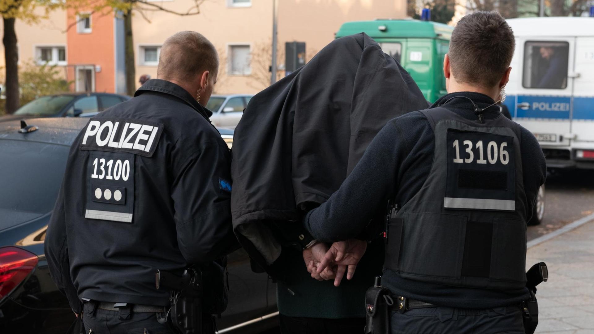 Bei einem Einsatz gegen arabischstämmige Clans in Berlin führen Polizeibeamte mit Handschellen einen festgenommenen Mann nach einer Razzia in einem Wohnhaus in Tempelhof ab. | Foto: Paul Zinken/dpa | Verwendung weltweit Bei einem Einsatz gegen arabischstämmige Clans in Berlin führen Polizeibeamte mit Handschellen einen festgenommenen Mann nach einer Razzia in einem Wohnhaus in Tempelhof ab. | Foto: Paul Zinken/dpa | Verwendung weltweit