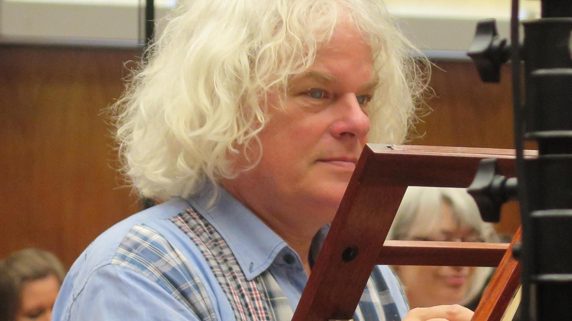 Ein älterer Mann mit mittellangen weißen Haaren sitzt in Seitenansicht vor einem Notenständer. Ein älterer Mann mit mittellangen weißen Haaren sitzt in Seitenansicht vor einem Notenständer.