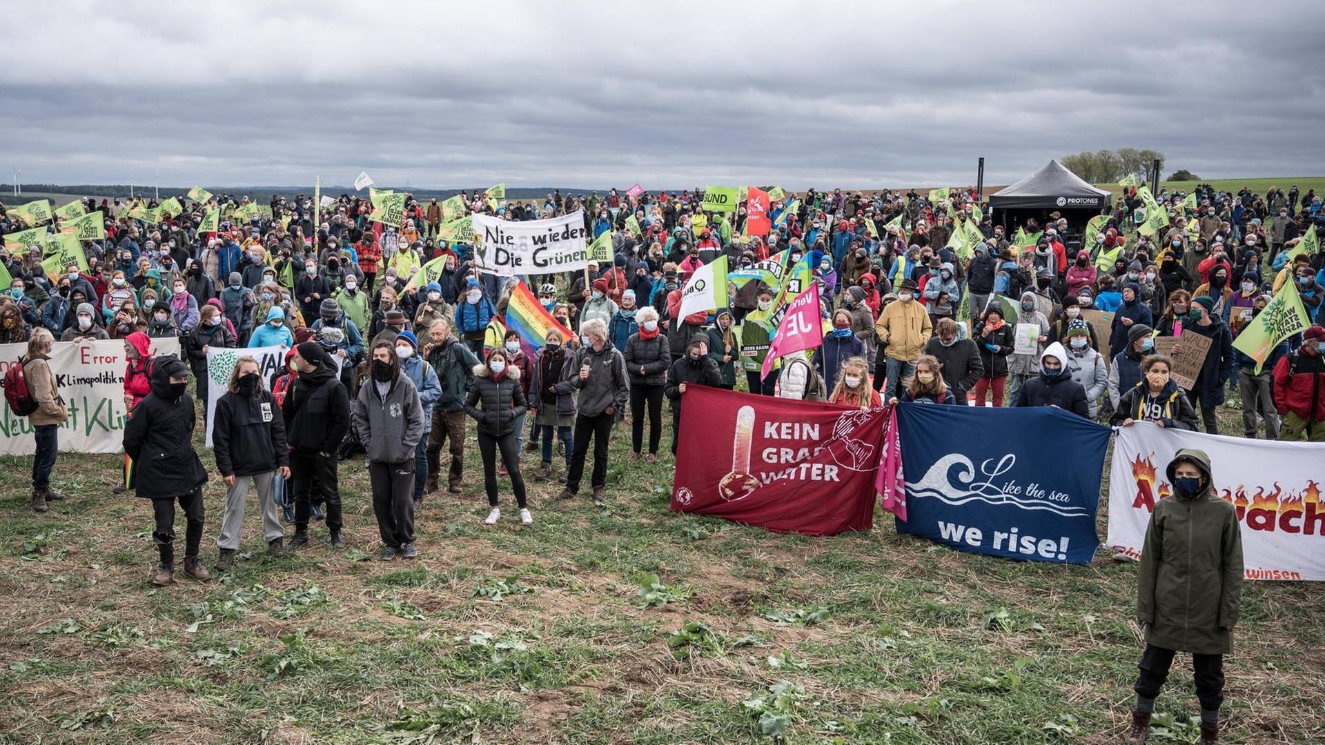 Demonstrantinnen und Demonstranten stehen mit Plakaten auf einer Wiese, darüber dunkle Wolken am Himmel. Demonstrantinnen und Demonstranten stehen mit Plakaten auf einer Wiese, darüber dunkle Wolken am Himmel.