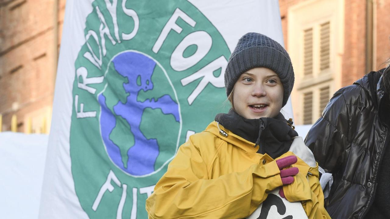 Die winterlich gekleidete Klimaaktivistin Greta Thunberg steht bei einer Kundgebung vor einer weißen Fahne, auf der das runde Logo "Fridays for Future" zu sehen ist. Im Hintergrund sind Häuser zu erkennen. Die winterlich gekleidete Klimaaktivistin Greta Thunberg steht bei einer Kundgebung vor einer weißen Fahne, auf der das runde Logo "Fridays for Future" zu sehen ist. Im Hintergrund sind Häuser zu erkennen.
