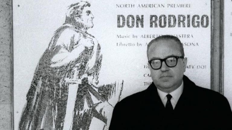 Am 21.12.1976 steht Alberto Ginastera in einem dunklen Mantel vor einem Plakat, das seine Oper "Don Rodrigo" ankündigt.