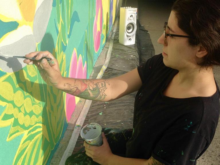 Estefanía Leighton sitzt auf der Straße und malt ein Street Art Bild