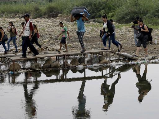 Männer, Frauen und Kinder gehen mit Gepäck an einem Fluss entlang