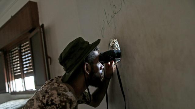 Ein Kämpfer der international anerkannten Regierung schaut mit einem Fernglas durch ein Einschussloch in einer Hauswand