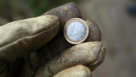 Eine Hand in einem Arbeitshandschuh hält eine Ein-Euro-Münze.