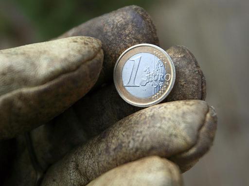 Eine Hand in einem Arbeitshandschuh hält eine Ein-Euro-Münze. Eine Hand in einem Arbeitshandschuh hält eine Ein-Euro-Münze.
