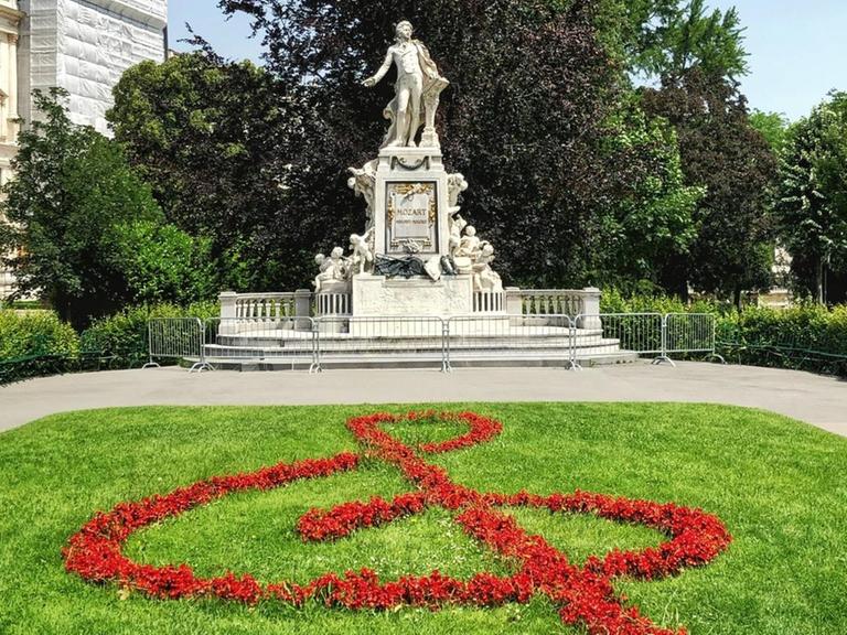 Blauer Himmel über dem Denkmal Mozarts im Park von Wien, vor dem aus roten Blumen ein Notenschlüssel gepflanzt wurde.
