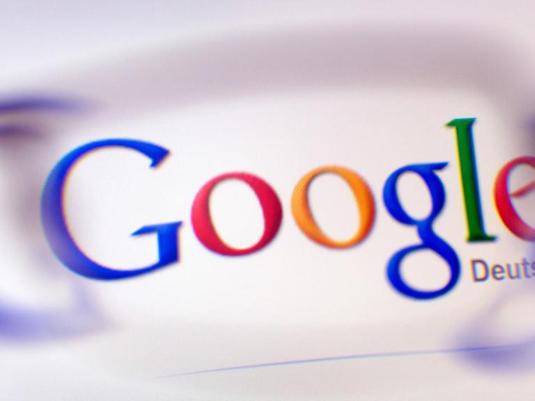 Das Google-Logo ist durch ein Brillenglas auf einem Bildschirm zu sehen.