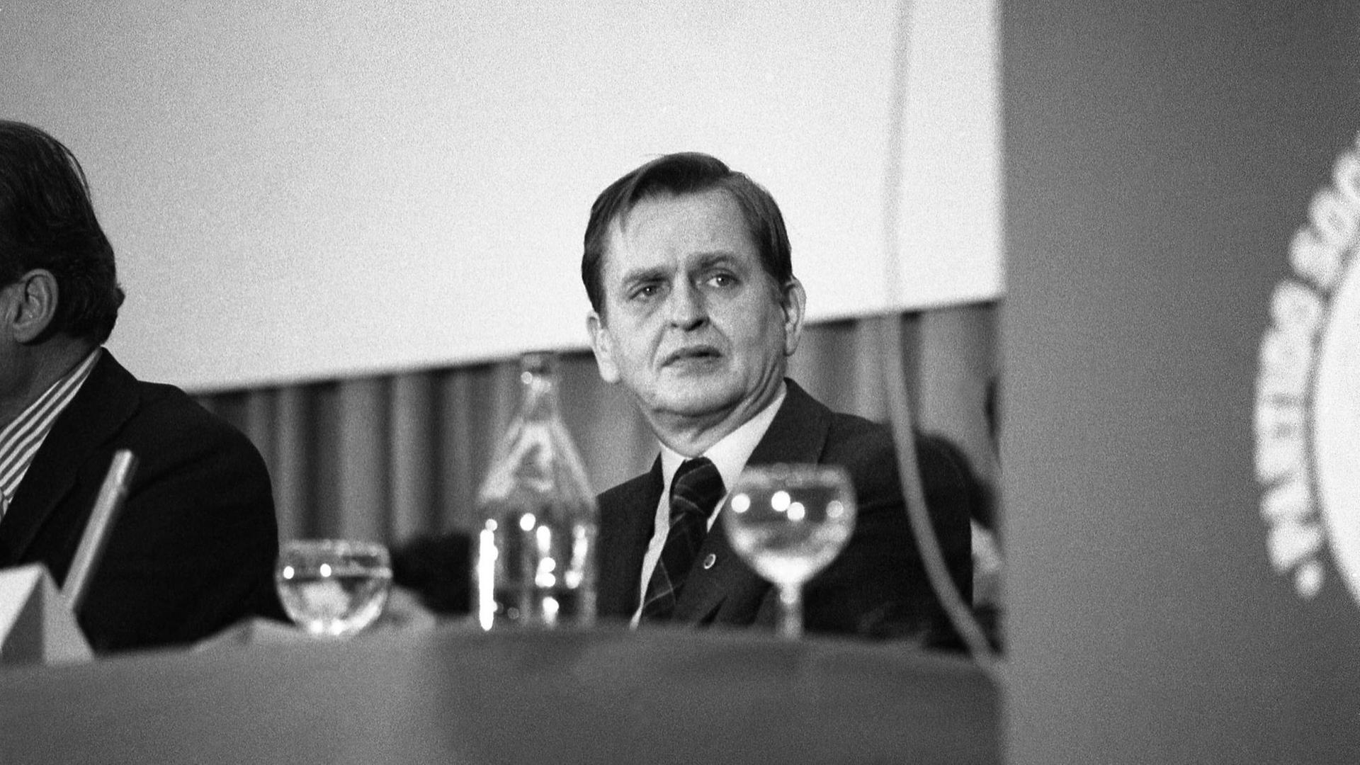 Olof Palme, bei einem Kongress am Tisch sitzend. Im Vordergrund Gläser.