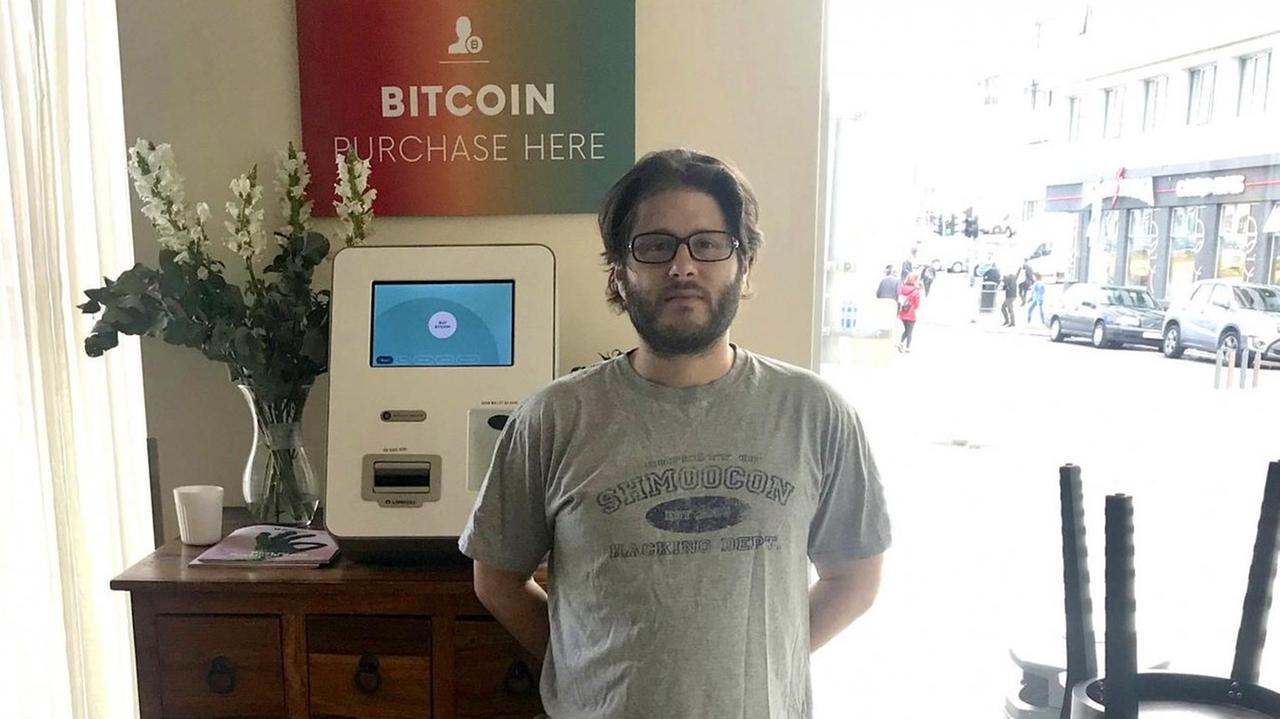Bitcoin-Unternehmer Jason Scott vor seinem Bitcoin-Automaten in Reykjavik. Ein kleiner, weißer Kasten mit Bildschirm.