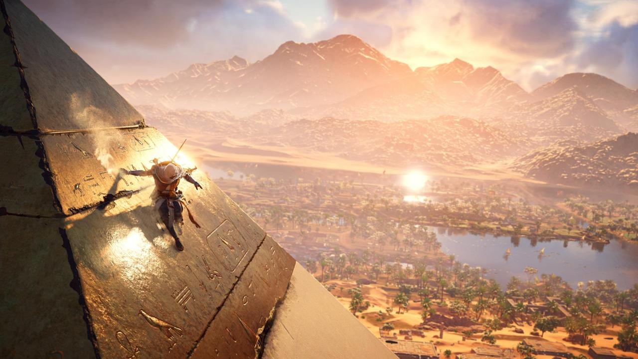 Eine Szene aus dem Computerspiel "Assassin's Creed Origins". Der Assassin rutscht eine Pyramide runter. Im Hintergrund sieht man eine Berglandschaft mit Oase Eine Szene aus dem Computerspiel "Assassin's Creed Origins". Der Assassin rutscht eine Pyramide runter. Im Hintergrund sieht man eine Berglandschaft mit Oase