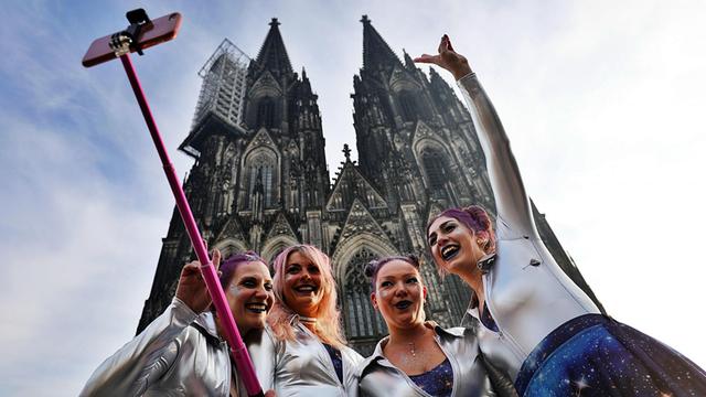 Vier kostümierte Frauen fotografieren sich mit einem Selfie-Stick an Weiberfastnacht 2018 vor dem Kölner Dom
