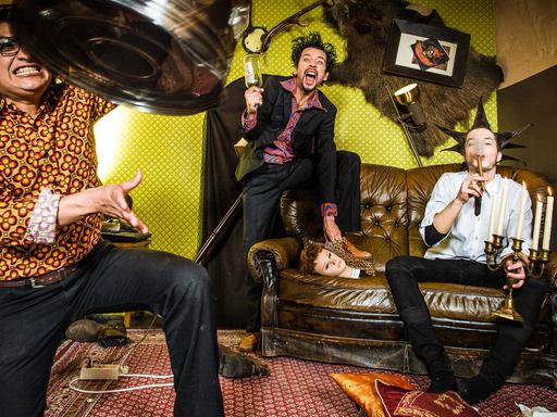 Foto der Kölner Band Chango Leon: Die Musiker posieren in exzentrischen Posen und farbenfroher Kleidung im Retro-Stil in einem ebenfalls in knalligen Farben im Retro-Stil gestalteten Raum.