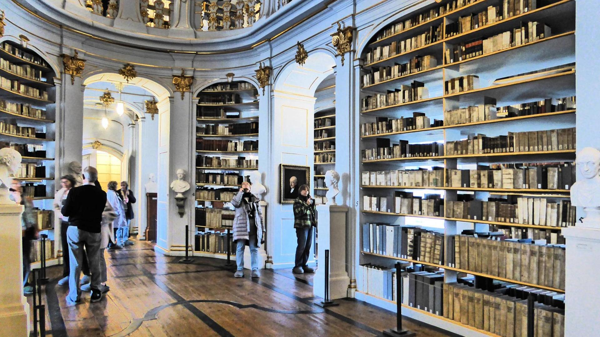 Blick in die Bibliothek mit Büchern auf Borden, stuckverzierten Wänden, Durchgängen und einer Empore Blick in die Bibliothek mit Büchern auf Borden, stuckverzierten Wänden, Durchgängen und einer Empore