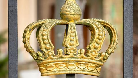 Eine goldfarbene Krone pragt als Zierde an einem barocken Zaun.