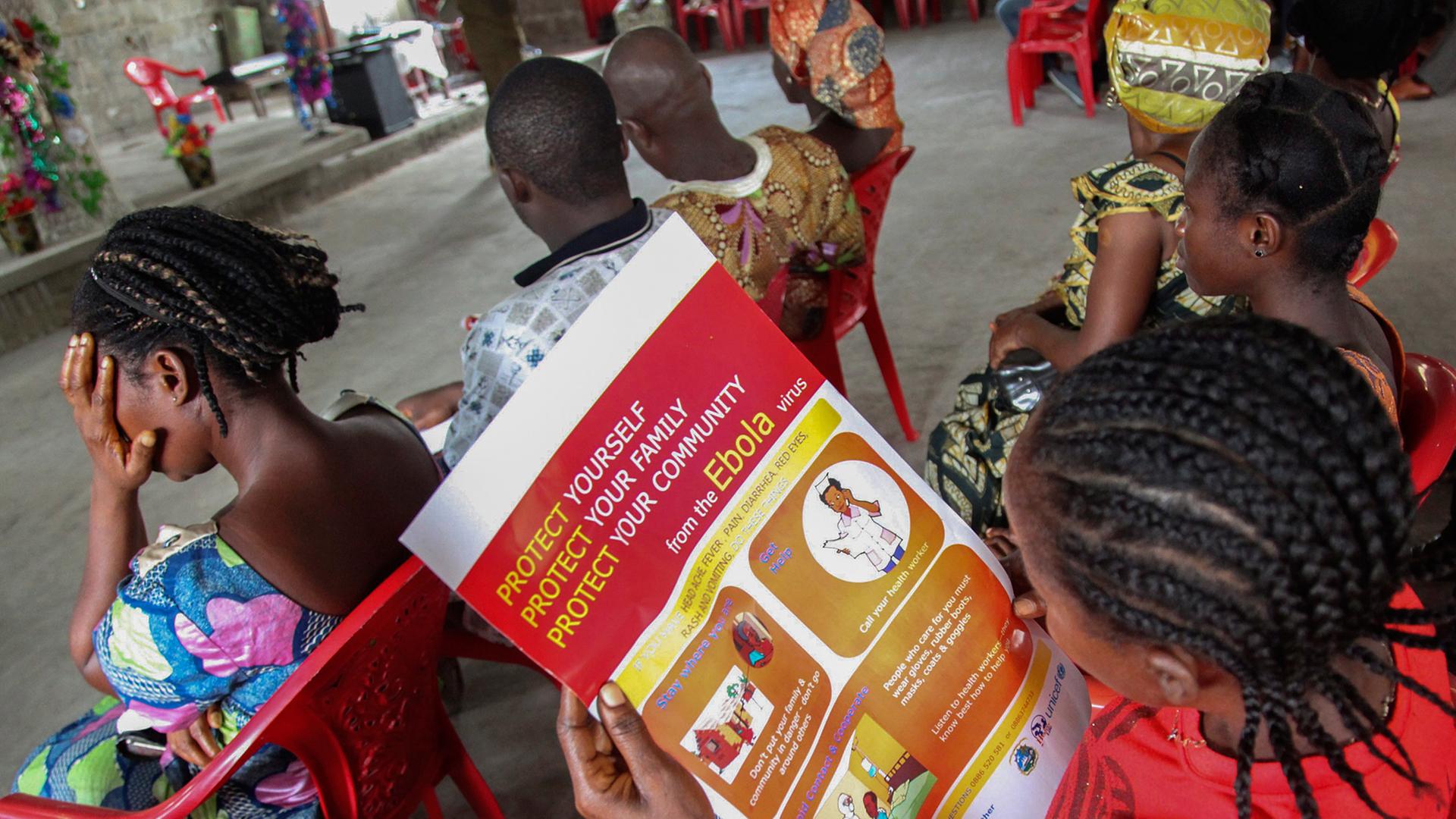 Frauen in Liberia sitzen auf Plastikstühlen und lesen Informationsblätter über den Schutz vor dem Ebola-Virus Frauen in Liberia sitzen auf Plastikstühlen und lesen Informationsblätter über den Schutz vor dem Ebola-Virus