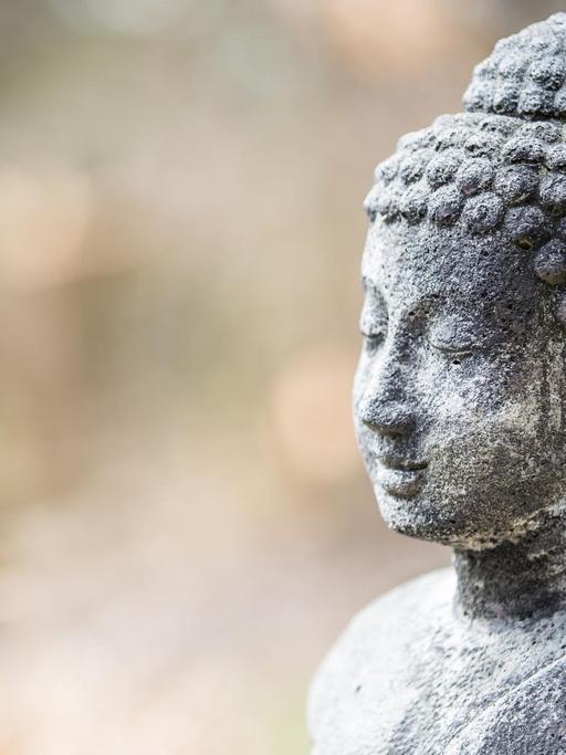Eine steinerne Buddha-Statue steht in einem Garten.