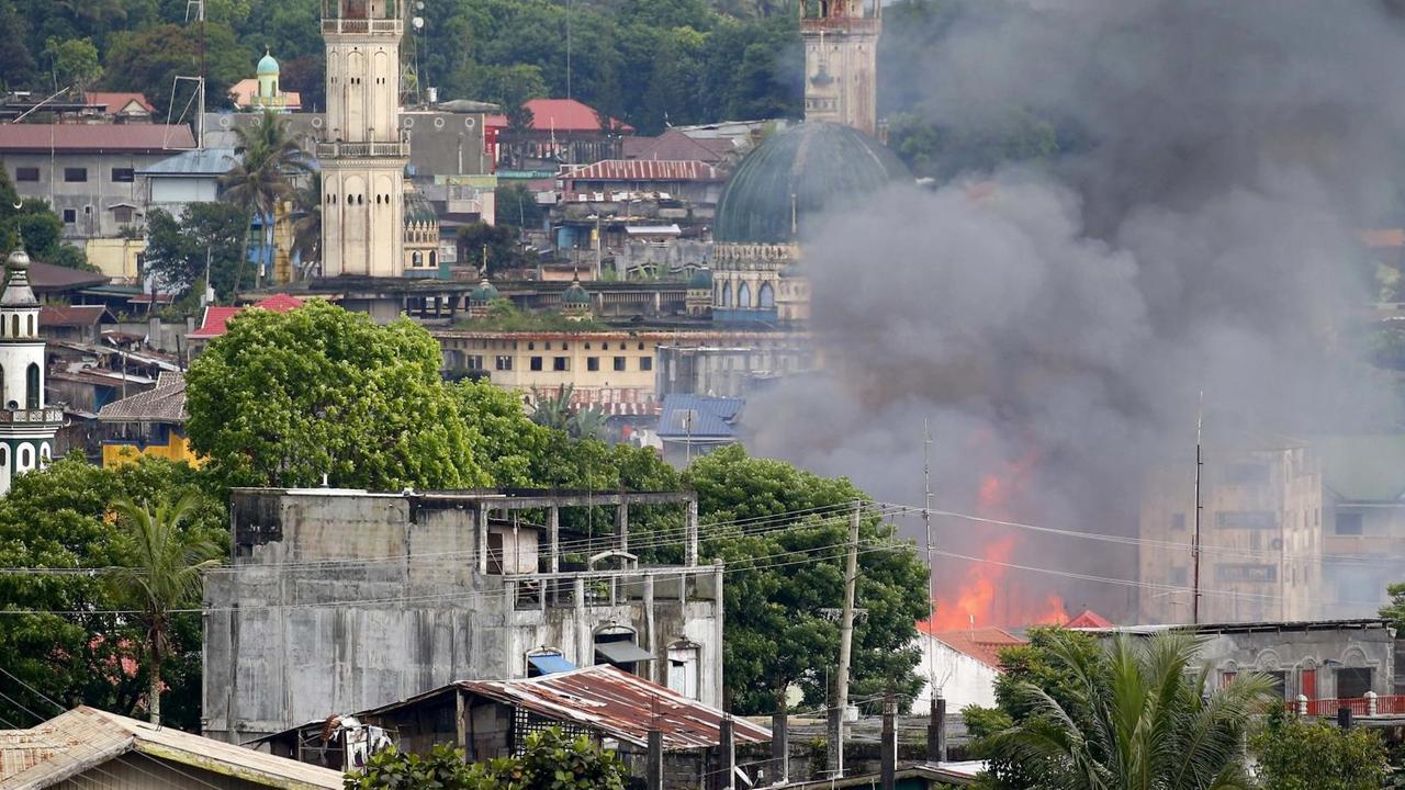 Das Bild zeigt einen Stadtteil, in dessen Mitte Gebäude brennen, aus denen dichter schwarzer Rauch aufsteigt. Das Bild zeigt einen Stadtteil, in dessen Mitte Gebäude brennen, aus denen dichter schwarzer Rauch aufsteigt.