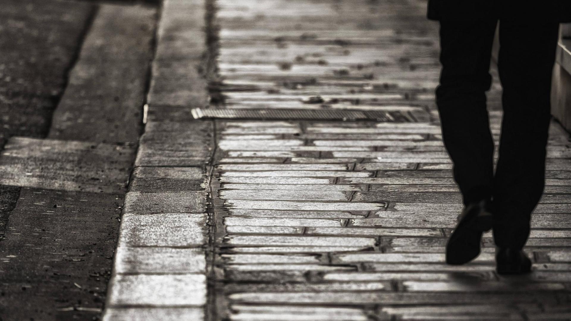 Ein Mann in schwarzer Kleidung läuft allein eine Straße entlang, nur die Beine und Schuhe sind sichtbar. Ein Mann in schwarzer Kleidung läuft allein eine Straße entlang, nur die Beine und Schuhe sind sichtbar.