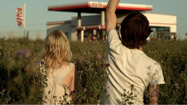 Die Zwillinge Elena (Julia Zange) und Robert (Josef Mattes) auf einer Wiese mit Blick auf eine Tankstelle im Hintergrund.