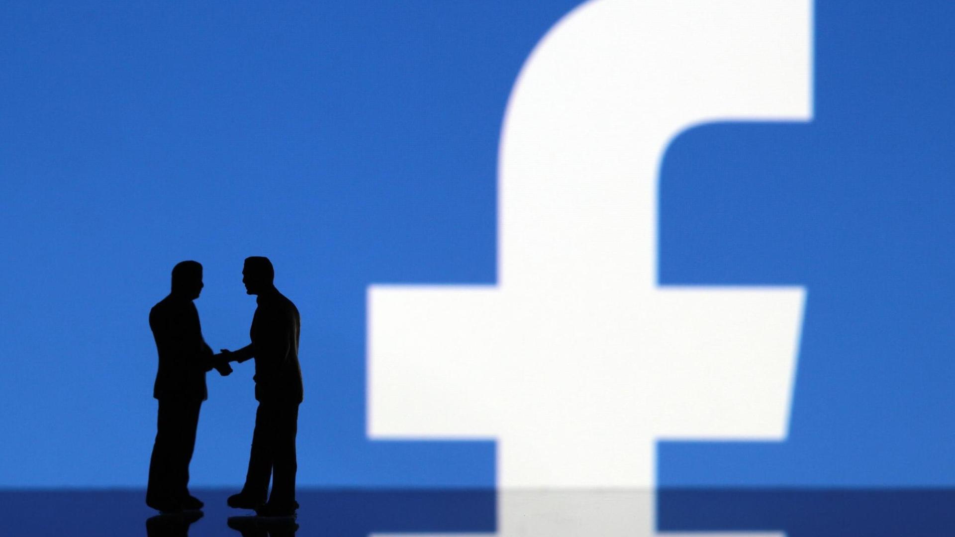 Miniaturfiguren geben sich die Hand vor einem Facebook-Logo. Miniaturfiguren geben sich die Hand vor einem Facebook-Logo.