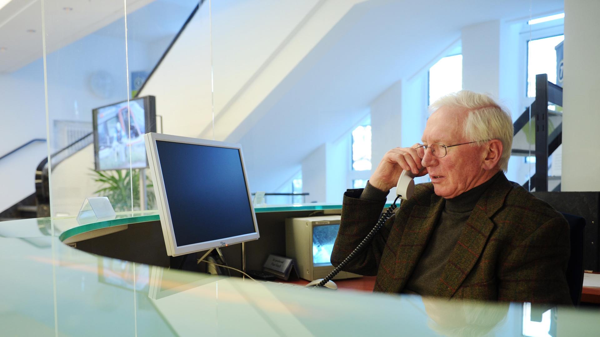 Ein Senior sitzt im Büro an einem Empfang und telefoniert. Ein Senior sitzt im Büro an einem Empfang und telefoniert.