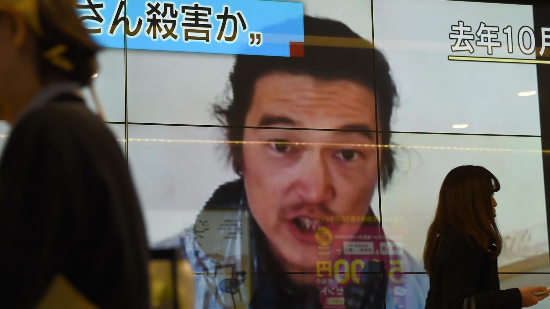 Passanten laufen an einer Leinwand vorbei. Zu sehen ist der Bericht über die Ermordung des japanischen Journalisten Kenji Goto.