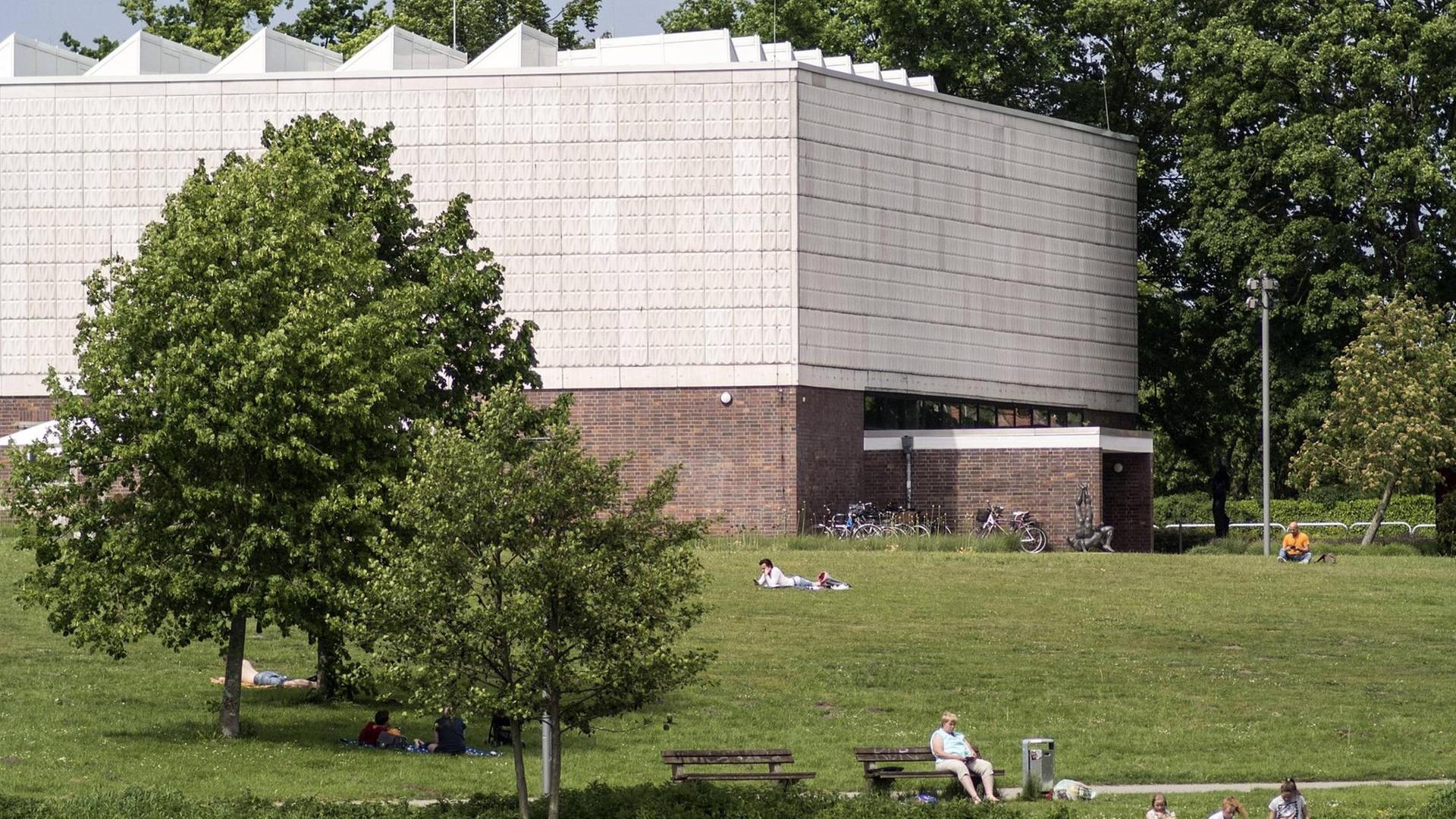 Parkanlage mit zwei Bäumen und Spaziergängern. Im Hintergrund die Kunsthalle Rostock, ein heller Bau ohne Fenster. Parkanlage mit zwei Bäumen und Spaziergängern. Im Hintergrund die Kunsthalle Rostock, ein heller Bau ohne Fenster.