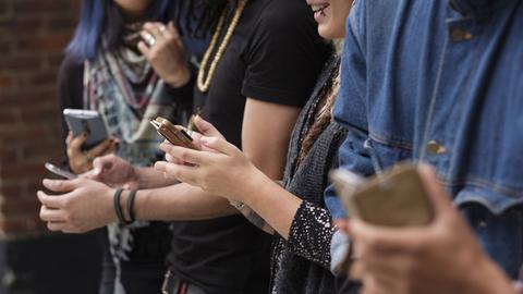 Junge Menschen stehen zusammen und nutzen ihre Smartphones.