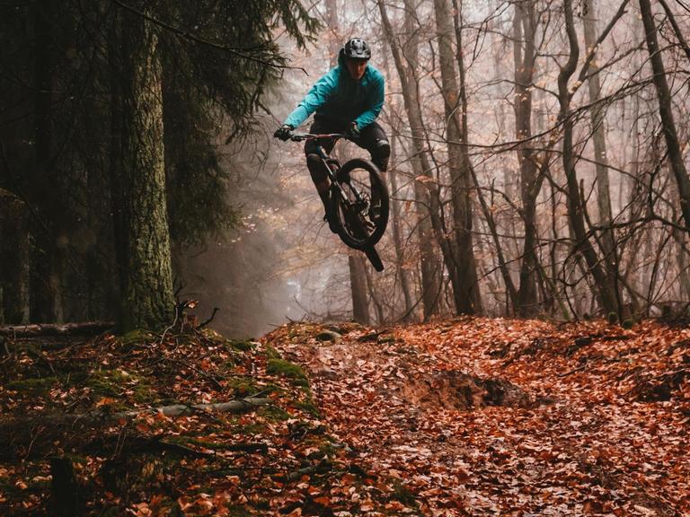 Ein Mountainbiker, der durch einen herbstlichen Wald fährt, im Sprung.