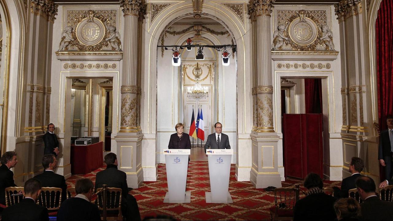 Bundeskanzlerin Merkel und Frankreichs Präsident Hollande stehen in einem prunkvollen Saal im Elysée-Palast in Paris an einem Stehpult. Bundeskanzlerin Merkel und Frankreichs Präsident Hollande stehen in einem prunkvollen Saal im Elysée-Palast in Paris an einem Stehpult.